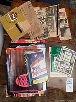 Image showing a pile of assorted vintage newspapers and souvenir booklets arranged on a wooden surface.