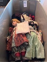 Box containing 7 porcelain head dolls dressed in vintage clothing, some paperwork included visible on top of dolls.