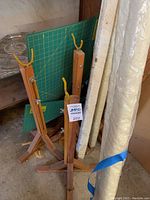 Four wooden adjustable quilting frame stands with yellow hooks at top, arranged near quilt rolls.