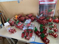 Wide shot of the collection of red Christmas trucks including pottery, ornaments, and holiday decorations arranged on a table.