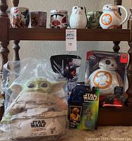 Star Wars mugs on a wooden rack, BB-8 and Porg themed items, Baby Yoda plush in package, Yoda figure, and BB-8 droid toy boxed with sound effects.