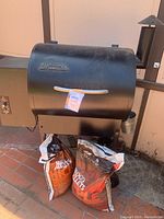Front view of grill with lid closed and two pellet bags at base