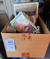 View of cardboard box labeled 'Wii' containing multiple Wii game cases and accessories including cords and remotes.