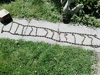 Full length of the steel tire chain laid out on grass and concrete, showing ladder pattern and rusted condition.