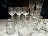 Assorted lead crystal glassware on display including goblets, vases, bowl, covered jar, and candlestick holders
