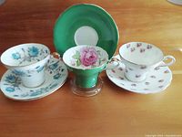 Overall view of three Aynsley corset shape teacups and saucers on wooden surface.
