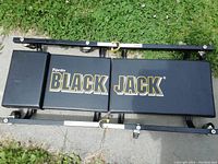 Top view of the Torin Black Jack creeper showing three padded sections with logo on grass and pavement background.