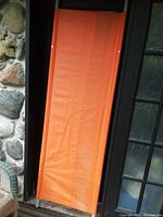 Photo of full orange fabric stretcher against a wall showing the fabric surface and metal frame.