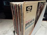Side view of multiple vintage vinyl LP albums in covers showing well worn condition. The Hits of Gerry and the Pacemakers album visible on front.