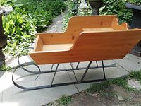 Side view showing the pine wood sleigh body with metal runners, outdoor garden background.