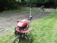 Angled front-left overview of tiller showing red engine housing and tines