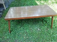 Full view of the rectangular coffee table positioned on grass showing wood veneer table top and wooden tapered legs.