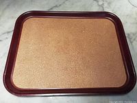 Full view of the rectangular Bakelite tray with cork surface sitting on a marble surface, showing the reddish-brown frame and textured cork center.
