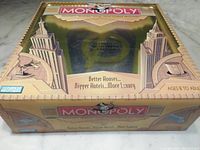 Monopoly game box with vintage art deco design and text about bigger houses, bigger hotels, and more luxury, suitable for ages 8 to adult.