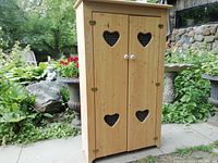 Front view of the pine wooden cupboard with two doors featuring heart-shaped cutouts with wire mesh.