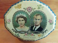 Top view of the octagonal toffee tin showing portraits of Queen Elizabeth II and Prince Philip with floral designs and scalloped edges