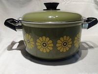 Front view of green enamel Dutch oven with yellow flowers and black handles on white background