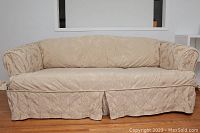 Front view of the 3-seater sofa covered in beige damask patterned slipcover showing overall shape and skirted bottom.