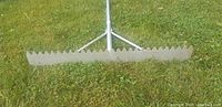 Close-up of 36-inch wide serrated aluminum rake head laying on grass.