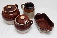 Photo showing four items: two single-handled bean pots with lids, a small pitcher, and a rectangular baking dish, all brown and tan in color.