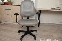 Front view of the grey vinyl upholstered task chair showing seat, backrest, armrests and caster base.