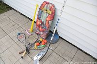 Wide view of the assorted children's sport items including racquets, balls, hockey sticks and inflatable punching bag.