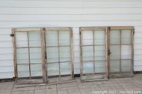 Front view of four wooden window panels with flaking paint and some broken/missing glass panes.