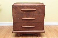 Full view of the vintage mid-century night stand showing all three drawers, wooden handles, cherry wood veneer with scratches and wear, and the wood grain finish.