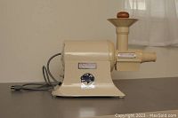 Side view of cream-colored Champion heavy duty juicer with wooden plunger and power cord visible.