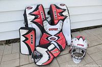 Complete set including pads, blocker, glove, chest protector, and mask arranged outdoors on pavement with white siding background.