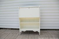 Front view of the white painted wooden secretary desk showing closed fold-down front panel and two open shelves below.