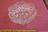 Clear Czech lead crystal bowl with detailed starburst and diamond-cut patterns, scalloped edge, and tripod feet photographed on a pink fabric surface with measurement indicators showing approximately 10 inches in diameter.