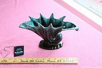 Ceramic snail-shaped vase on pink fabric surface with a wooden ruler for size reference and hanging Blue Mountain Pottery tag visible.