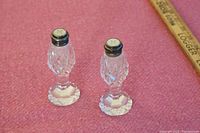 Pair of crystal salt and pepper shakers shown on pink fabric background, highlighting cut crystal detail and silver caps.