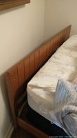 Close-up side view of wooden paneled headboard and part of foam mattress with floral sheets.