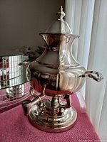 Front and side view of the elegant silverplated coffee urn showing its reflective surface, handles, and base burner.
