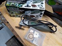 Genesis oscillating tool with power cord next to its original box and a plastic container holding various blades and grinding accessories.