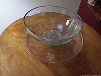 View of glass bowl and plate on wooden table showing floral etched design and the shape and clarity of glass.