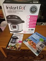 Photo of the boxed Instant Pot IP-DUO60 V3 showing the packaging and two recipe books on a wooden table.