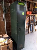 Single tall metal locker with Indian City branding, located in storage area with cardboard boxes and other items around.