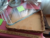 9x13 Pyrex glass casserole dish resting on woven carrier with leather handles, placed on a table with a sticky note indicating '9x13'.