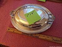 Top and side view of oval silver plated serving tray with lid and decorative handles, measuring 11 x 9 inches.