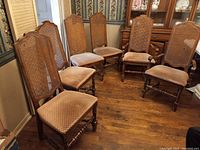 Six wooden highback chairs arranged in a semi-circle showing woven cane backs and beige upholstered seats.