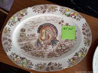 Top view of an oval ceramic turkey platter measuring 18.5 by 14 inches, featuring a colored turkey illustration and a fruit-decorative border.