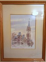 Framed watercolor print 'The Parliament Buildings' by Diane Ottens with light wood frame and matting, visible architectural details of the Parliament tower and nearby buildings in winter scene.