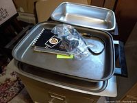 Open skillet viewed from above showing non-stick cooking surface, instruction manuals, and power cord wrapped in plastic on the cooking surface.