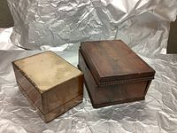 Two wooden keepsake boxes side by side, showing top and side views. Larger box with scrolled edges, smaller box shows inlaid wood top. Both show visible wear and discoloration.
