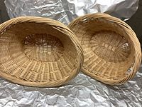 Two oval wicker laundry baskets shown side by side, displaying woven wicker construction and rounded rims.