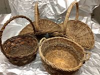 Photo of four wicker baskets on a white crumpled surface, showing shapes, sizes, and handle styles.