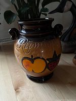 Close-up of brown Rumtopf crock showing fruit decoration and embossed lettering on glazed ceramic.